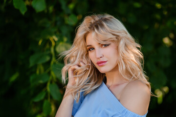 Naklejka premium Portrait of a young beautiful girl 21 years old in a blue summer dress with a white belt bag. The woman smiles. Beautiful lips and eyes. Long loose hair.
