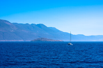 Beautiful seascape with calm blue Mediterranian sea, mountains in mist and boat, touristic season, vacation on sunny islands