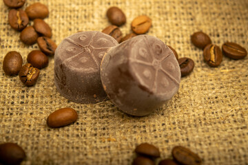 Chocolate, coffee beans and chunks of brown cane sugar on a background of homespun fabric with a rough texture. Close up.