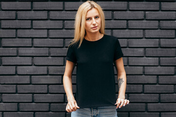 Fototapeta na wymiar Stylish blonde girl wearing black t-shirt and glasses posing on black wall background, urban clothing style. Street photography