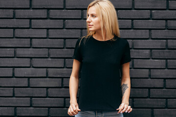 Stylish blonde girl wearing black t-shirt and glasses posing on black wall background, urban...
