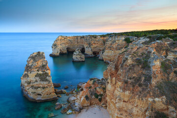 Algarve in Portugal and its amazing beaches, is a summer holiday destination for many tourists in Europe. Landscape with cliffs on the coast at colorful sunset. Pure nature, blue sea, sand.