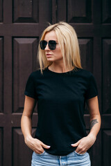 Stylish blonde girl wearing black t-shirt and glasses posing against street , urban clothing style....