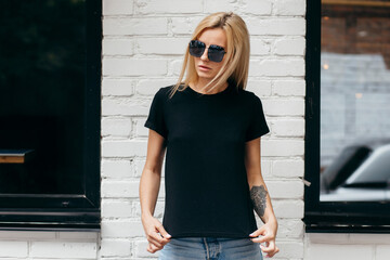 Stylish blonde girl wearing black t-shirt and glasses posing against street , urban clothing style....