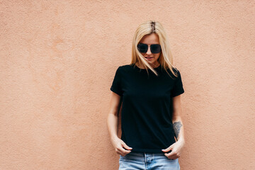 Stylish blonde girl wearing black t-shirt and glasses posing against street , urban clothing style....
