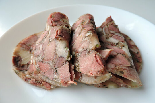 Some slices of home made head cheese on a white plate, white background
