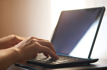 Hand of a woman typing on the Bluetooth keyboard that connected to a tablet