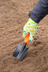 Hand Female In Work Glove With Garden Scoop In Soil Ground In Garden Outdoor In Spring Close Up.