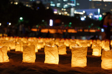 A field of candlelit paper lanterns on Odaiba Beach with city lights visible in the background