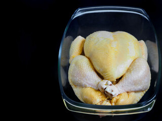 raw large yellow corn fattening chicken carcass in a transparent glass bowl on a black background