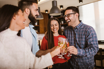 Young people cheering with champagne flutes and looking happy while having home party.