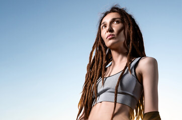 slim girl with dreadlocks in a short top and trendy jeans in the sunset