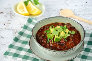Homemade vegan black bean chili tomato soup with diced avocado and chopped parsley served with lemon