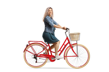Obraz premium Side shot of a young woman in a dress riding a red bicycle and looking at the camera