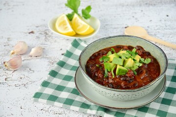 Homemade vegan black bean chili tomato soup with diced avocado and chopped parsley served with lemon