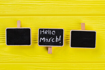 Three small nameplates on a yellow wooden table. Hello march concept.