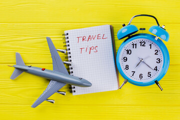 Flat lay travel tips concept. Plastic airplane with notepad and alarm clock on yellow wood.