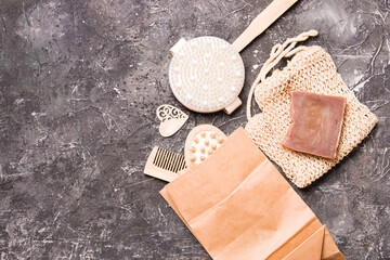 dry anti-cellulite massage brush, knitted cotton sponge, natural cocoa soap and a paper bag with a wooden comb and a body massager on a black background, copy space