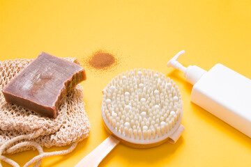 white foacon with dispenser without a label, a brush for dry massage, a piece of homemade chocolate soap and a knitted washcloth and a handful of ground coffee on a yellow background