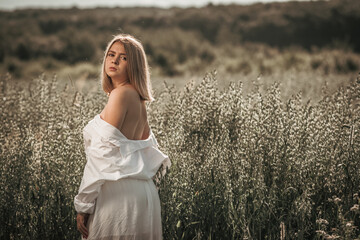 Fototapeta na wymiar Young busty girl in a white dress on an oat field.