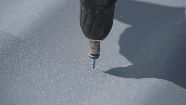 Twisting the roof self-tapping screw into the metal tile. Close up.