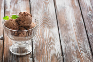 Chocolate ice cream balls in a glass bowl on a wooden dark rustic background. Summer refreshing dessert. Side view, selective focus, copy space.