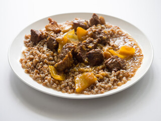 Hungarian goulash. Buckwheat with beef. White round plate on a white background