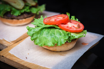 Burger Beef , tomatoes, red onions, cucumber and lettuce on black slate over dark background. Unhealthy food