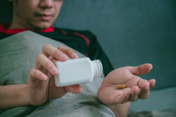Sick asian man is pouring medicine out of a medicine bottle into the hand
