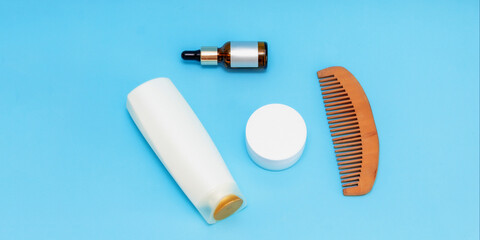 white round cream jar, pipette jar, wooden comb, large white bottle are on a blue sky background, the view from the top