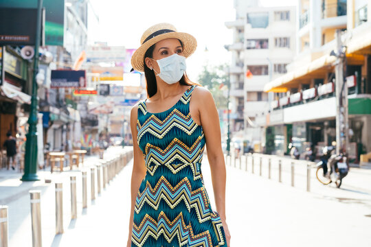 Young brunette woman traveling in Bangkok, Thailand in popular Khao San Road during pandemic Coronavirus. 20s Hispanic in a protective mask wear summer sleeveless summ dress in Asia. With Copy space