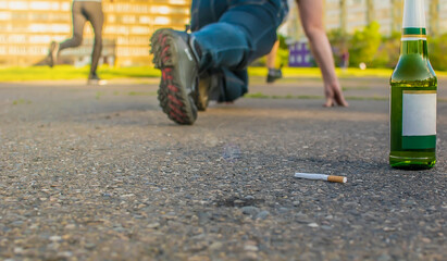 a discarded cigarette lies near a beer bottle on the asphalt path next to a man who is preparing to run a sprint through the city stadium