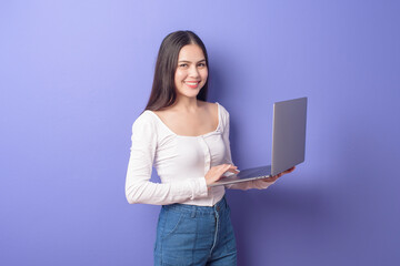 portrait of young beautiful smiling woman is holding laptop over isolated purple background studio