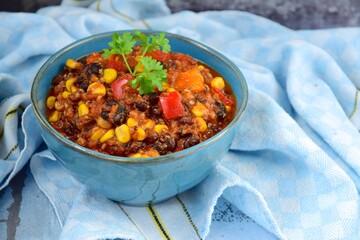 Black bean, quinoa, sweet potato, bell pepper and corn chili in a bowl garnish with parsley