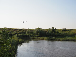 Fototapeta na wymiar military helicopter flies over a field and a lake