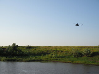 Obraz na płótnie Canvas military helicopter flies over a field and a lake