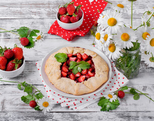 Shortbread galette with strawberry surrounded by berries and chamomiles on the white wooden table