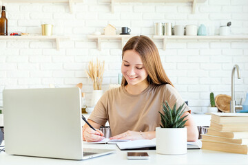 Smiling female teenager studying at the laptop at home