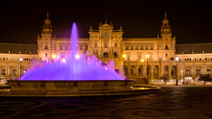 Fototapeta na wymiar Purple Fountain - A wide-angle night view of the illuminated water fountain at the center of Spanish Square - Plaza de España, Seville. Andalusia, Spain.