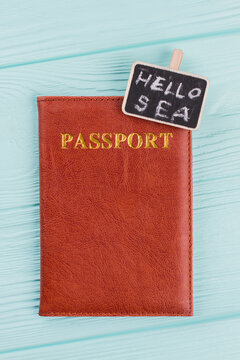 Brown leather passport on blue wooden background. Hello sea written on nameplate.