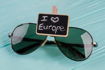 Black eyeglasses on a wooden background. I love europe written on nameplate near sunglasses.