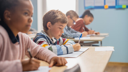 In Elementary School Classroom Brilliant Black Girl Writes in Exercise Notebook, Taking Test and...