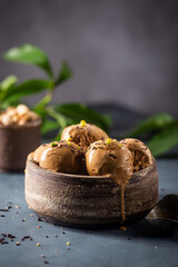 Scoops of coffee or chocolate ice cream in a bowl with green leaves on dark background