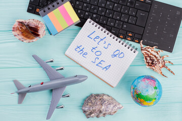 Summer travel accessories consist of seashells, airplane, globe on blue background. Let's go to Sea on notebook.