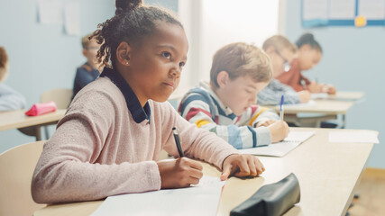 In Elementary School Classroom Brilliant Black Girl Writes in Exercise Notebook, Taking Test and...