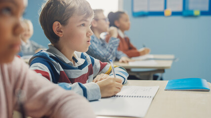 In Elementary School Class: Portrait of Brilliant Caucasian Boy Writes in Exercise Notebook, Taking...