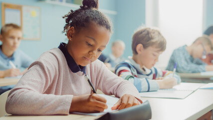 In Elementary School Class: Portrait of a Brilliant Black Girl with Braces Writes in Exercise Notebook, Smiles. Junior Classroom with Diverse Group of Children Learning New Stuff - obrazy, fototapety, plakaty