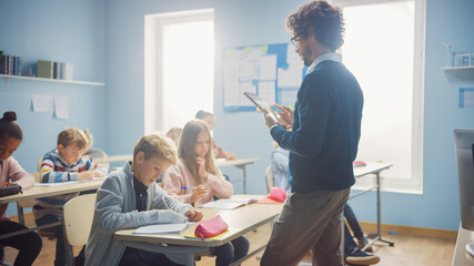 Teacher Uses Digital Tablet Computer While Explainin a Lesson to a Classroom Full of Diverse...