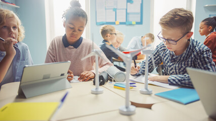 In the Elementary School: Class of Brilliant Young Children Work as a Team Using Tablet Computers to Program Wind Turbines. Classroom with Kids Learning about Eco-Friendly Forms of Renewable Energy