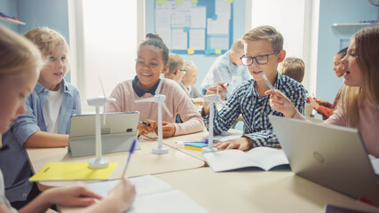 Fototapeta premium In the Elementary School: Class of Smart Young Children Work as a Team Using Tablet Computers to Program Wind Turbines. Classroom with Kids Learning about Eco-Friendly Forms of Renewable Energy